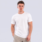 A man wearing a plain white short-sleeve t-shirt and light beige trousers, standing against a solid light gray background.